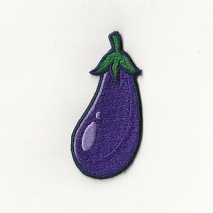 May include: A purple eggplant with a green stem, embroidered on a white fabric background.