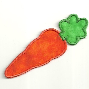 以下が含まれることがあります： フェルトのニンジンのアップリケで、緑色のフェルトの葉が上に付いています。ニンジンはオレンジ色で、葉は緑色です。