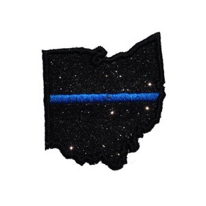 Puede incluir: Esquema del estado de Ohio en purpurina negra con una fina línea azul en el medio.