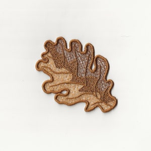 Puede incluir: Una aplicación de encaje marrón y beige en forma de hoja de roble.