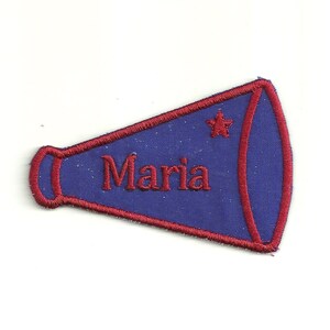 Puede incluir: Parche bordado azul y rojo con forma de megáfono. El nombre "Maria" está bordado en rojo dentro del megáfono, con una estrella roja en el lateral. Este parche es probablemente para una animadora o un equipo deportivo.
