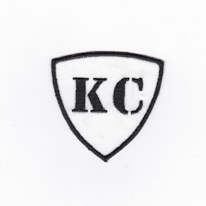 Peut inclure: Écusson brodé blanc avec des coutures noires en forme de bouclier avec les lettres "KC" au centre.