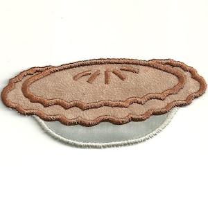 May include: A brown and white embroidered patch of a pie with a flaky crust.