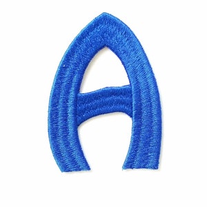 Może przedstawiać: Wyhaftowana niebieska litera A. Litera wykonana jest z grubego, niebieskiego sznurka i ma lekko zaokrąglony kształt.