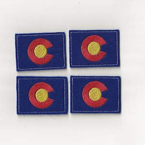 May include: Four blue felt patches with the embroidered state flag of Colorado. The flag features a large gold circle with a red 'C' inside.