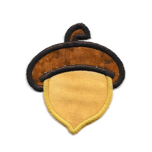 Könnte beinhalten: Eine braune und gelbe Filz-Eichel-Applikation mit schwarzem Umriss.