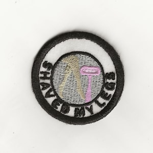 May include: A white and black circular patch with the text "Shaved My Legs" in a black circle around a gray background with a tan outline of legs and a pink razor.