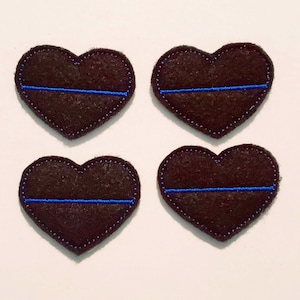 Könnte beinhalten: Vier herzförmige Patches aus braunem Filz mit einer dünnen blauen Linie, die quer über die Mitte gestickt ist.