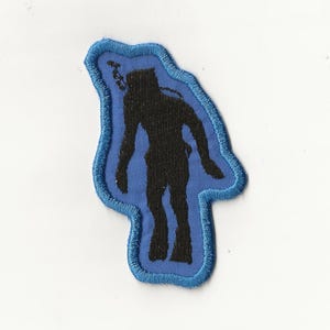 Könnte beinhalten: Ein blau-schwarzer, gestickter Aufnäher mit einer Taucher-Silhouette. Der schwarze Taucher steht vor einem blauen Hintergrund und ist von einem blauen Rand umgeben. Ideal für Jacken oder Taschen.