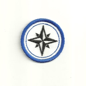 May include: A white oval patch with a blue border and a black compass rose in the center.