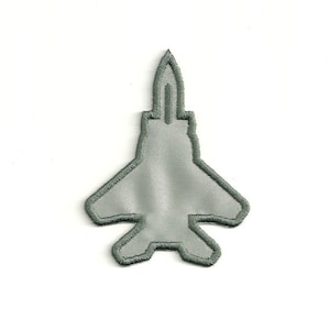 Op de afbeelding: Een grijs geborduurd patch in de vorm van een straaljager.