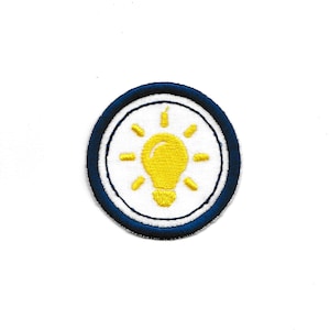 May include: A blue and white embroidered patch with a yellow light bulb in the center. The light bulb has a white filament and rays of light.