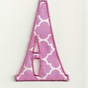 Op de afbeelding: Roze stoffen letter A met een wit geometrisch patroon. De letter is uitgesneden en heeft een gestikte rand.