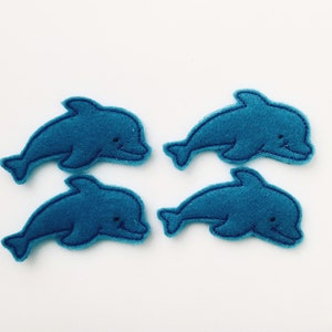 May include: Four blue felt dolphin shapes, each with a simple embroidered face. These felt shapes are perfect for crafts or decorations.