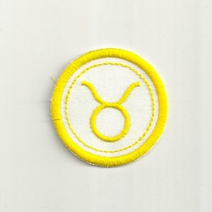 May include: Yellow embroidered Taurus zodiac sign patch with a white background and a yellow outer border.