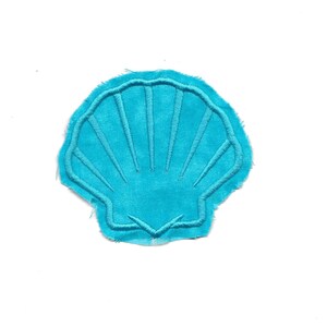 Pode incluir: Um remendo de tecido em forma de concha de cor azul turquesa com contorno branco. A concha tem um design bordado detalhado.