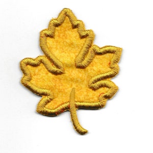 May include: A gold embroidered maple leaf patch. The leaf is outlined in gold thread and has a textured, slightly fuzzy surface.