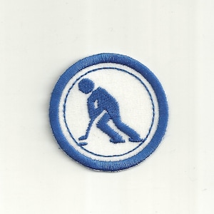 Puede incluir: Un parche bordado azul y blanco con una silueta estilizada de una persona jugando al hockey.