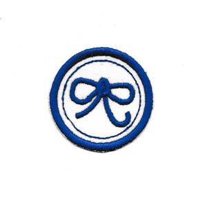 May include: A blue embroidered patch with a white circle and a blue bow in the center.