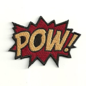 Può includere: Una toppa ricamata rossa e dorata con la parola "POW!" in stile fumetto.