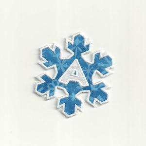 Puede incluir: Un parche de tela azul en forma de copo de nieve con costuras blancas y la letra "A" en el centro.