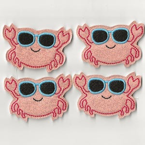 Op de afbeelding: Vier roze krabpleisters met zwarte zonnebrillen en blauwe monturen. De krabpleisters hebben een lachend gezicht en rode geborduurde details. Perfect om een leuke, strandachtige sfeer toe te voegen aan kleding of accessoires.
