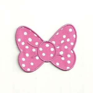 May include: Pink fabric bow with white polka dots. The bow is a flat, iron-on patch.