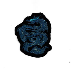 以下が含まれることがあります： 黒い背景に青い刺繍のドラゴンパッチ。ドラゴンは頭を右に向けて円形に丸まっています。