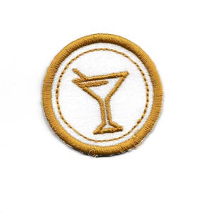 May include: Circular embroidered patch with a gold cocktail glass design on a white background. The patch has a gold border and a stitched appearance. Perfect for adding a touch of flair to clothing or accessories.