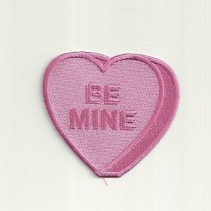 May include: Pink felt heart-shaped patch with the words "BE MINE" embroidered in white.