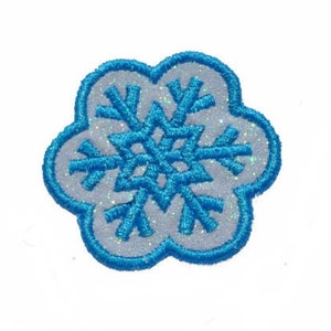 May include: A blue snowflake embroidered patch with a white glitter background. The snowflake is in a flower shape.