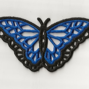 Puede incluir: Un parche de bordado de mariposa azul con contorno negro. La mariposa tiene intrincados detalles de alas.