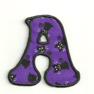 May include: Purple felt letter A with black cat print. The letter is outlined in black thread.