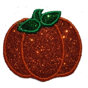 Puede incluir: Una calabaza naranja brillante con hojas de purpurina verde. La calabaza es una decoración festiva para el otoño.
