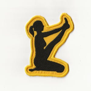 May include: A yellow embroidered patch featuring a black silhouette of a person performing a yoga pose.