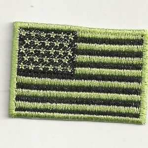 May include: A green and black embroidered American flag patch. The stars are green and the stripes are black and green.