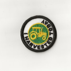 May include: A black and white circular patch with a green circle in the centre. The green circle has a yellow tractor with the words "JOHN DEERE" around the outside.