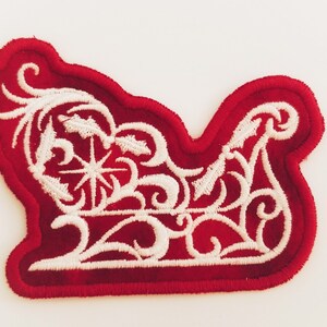 Peut inclure: Patch de traîneau de Noël en feutre rouge avec des détails brodés blancs. Le traîneau est décoré d'un flocon de neige et de vignes en spirale.