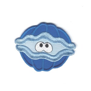 May include: A blue embroidered patch in the shape of an oyster shell with a cartoon face. The shell is a darker blue with lighter blue wavy lines. The face has two black eyes and a light blue background.