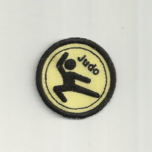 May include: A black and yellow embroidered patch with a stick figure performing a judo move and the word "Judo" written in black.