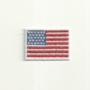 Op de afbeelding: Geborduurde patch met de Amerikaanse vlag. De patch heeft een blauw vierkant met witte sterren in de linkerbovenhoek en rood-witte strepen. De patch is rechthoekig en heeft een witte rand.