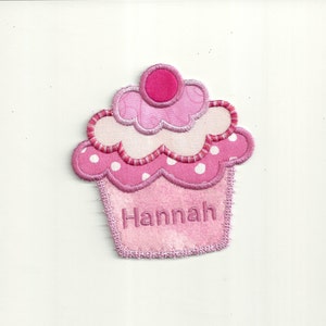 May include: Pink cupcake-shaped fabric patch with white polka dots and the name "Hannah" embroidered on the front.