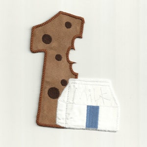 Puede incluir: Un número uno de fieltro marrón con lunares marrones y un mordisco. Un cartón de leche de fieltro blanco con fieltro azul en la parte superior y la palabra "Leche" escrita en él.