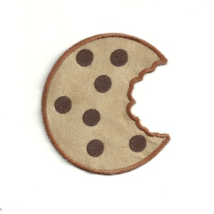 May include: A brown and tan felt cookie with a bite taken out of it. The cookie has brown chocolate chips on it.
