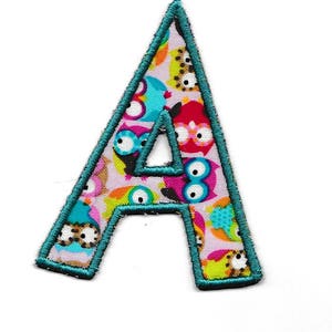 Op de afbeelding: Een teal stoffen letter A met een kleurrijke uilprint. De letter is omrand met teal.