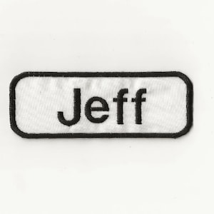 May include: White rectangular name tag with black border and black embroidered text that reads "Jeff".