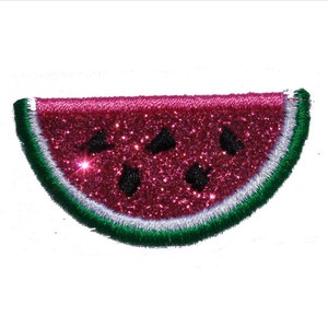 Puede incluir: Una rebanada de sandía rosa con bordes verdes y blancos, hecha de tela brillante. La sandía tiene semillas negras.