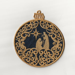 May include: A gold embroidered Christmas bauble with a blue background featuring a nativity scene with a star above the manger. The bauble is shaped like a circle with a loop at the top.