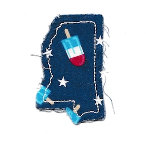 Pode incluir: Um remendo de tecido azul em forma do estado do Mississippi com estrelas brancas e uma ilustração de um picolé vermelho, branco e azul.