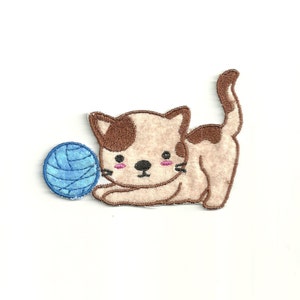 Peut inclure: Un chat de dessin animé brun et blanc avec des joues roses jouant avec une pelote de laine bleue. Le chat est couché sur le ventre, la queue enroulée.
